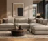 Interior shot of a modern living room featuring large L-shaped sofas (ركنات مودرن) in a light beige fabric. The sofas are decorated with brown and patterned pillows and are arranged around a low, round wooden coffee table with a central vase. The background includes a large abstract painting and two indoor trees