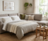 A photorealistic interior design photograph of a modern living room featuring a compact, stylish L-shaped corner sofa bed in warm greige upholstery. The pull-out bed function is partially extended with neat pillows and a cozy blanket, demonstrating its transformation into a comfortable sleeping space. The scene includes a small wooden nesting coffee table, subtle ambient lighting, minimalist minimalist decor, and a natural light-filled atmosphere tailored for small spaces ركنة مودرن سرير